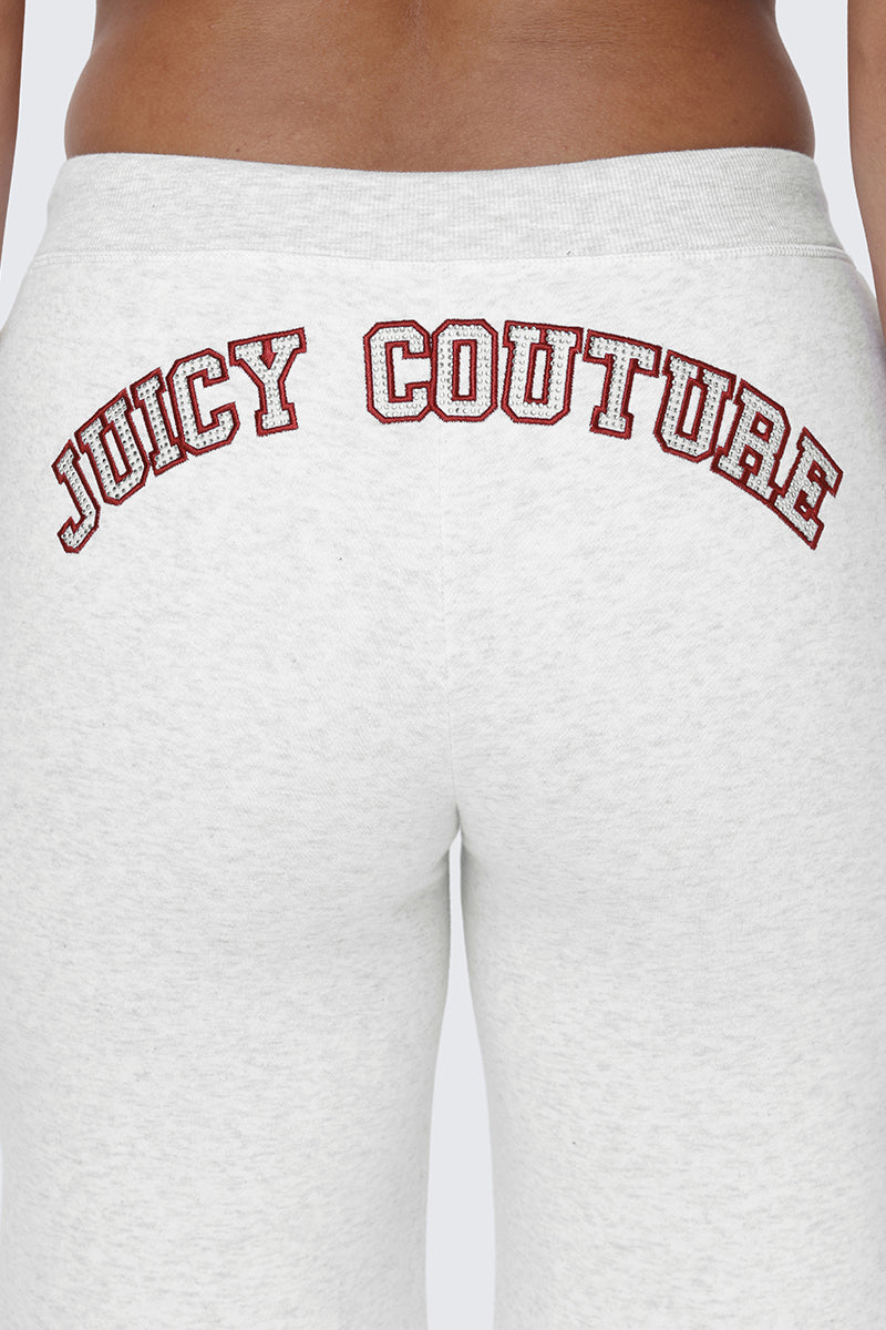 A close-up of a person wearing the Small Bling Fleece Wide Leg Pants in light gray, featuring a comfortable drawstring waistband, a rhinestone Juicy logo, and JUICY COUTURE written in bold red and white letters across the back.