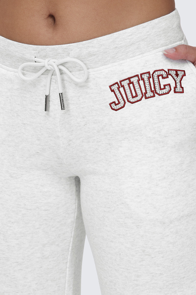 Close-up of a person wearing the Small Bling Fleece Wide Leg Pants in light gray, featuring a drawstring waistband and "JUICY" printed in red with a white outline on the hip. One hand with pink nails rests on the waistband.