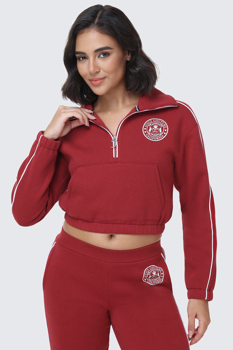 Model dressed in the Scottie Fleece Quarter Zip Sweatshirt—featuring a matching maroon set with a zippered collar, white sleeve piping, and Scottie crest graphics on both the top and pants—posed against a simple light background.