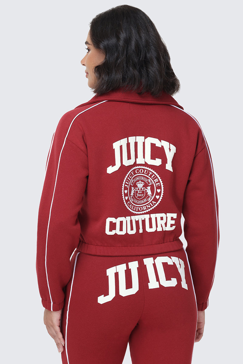 A woman wearing a red Scottie Fleece Quarter Zip Sweatshirt by Juicy Couture with white lettering and the Scottie crest graphic logo on the back is facing away from the camera. She also has JUICY written across the back of her pants.