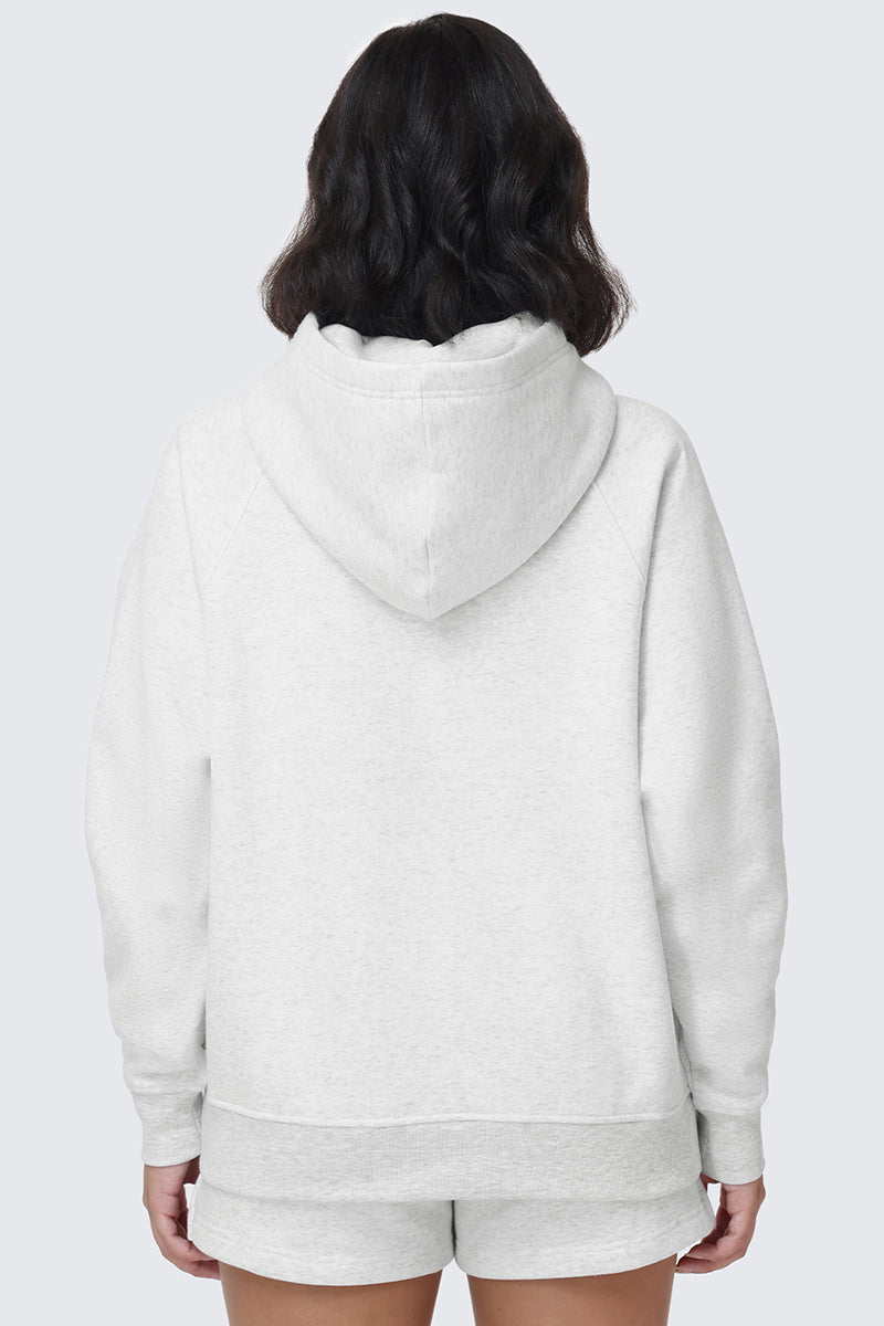 A person with shoulder-length dark hair is shown from the back, wearing the Scottie Fleece Oversized Hoodie in white featuring the Juicy crest, paired with matching white shorts, against a plain light background.