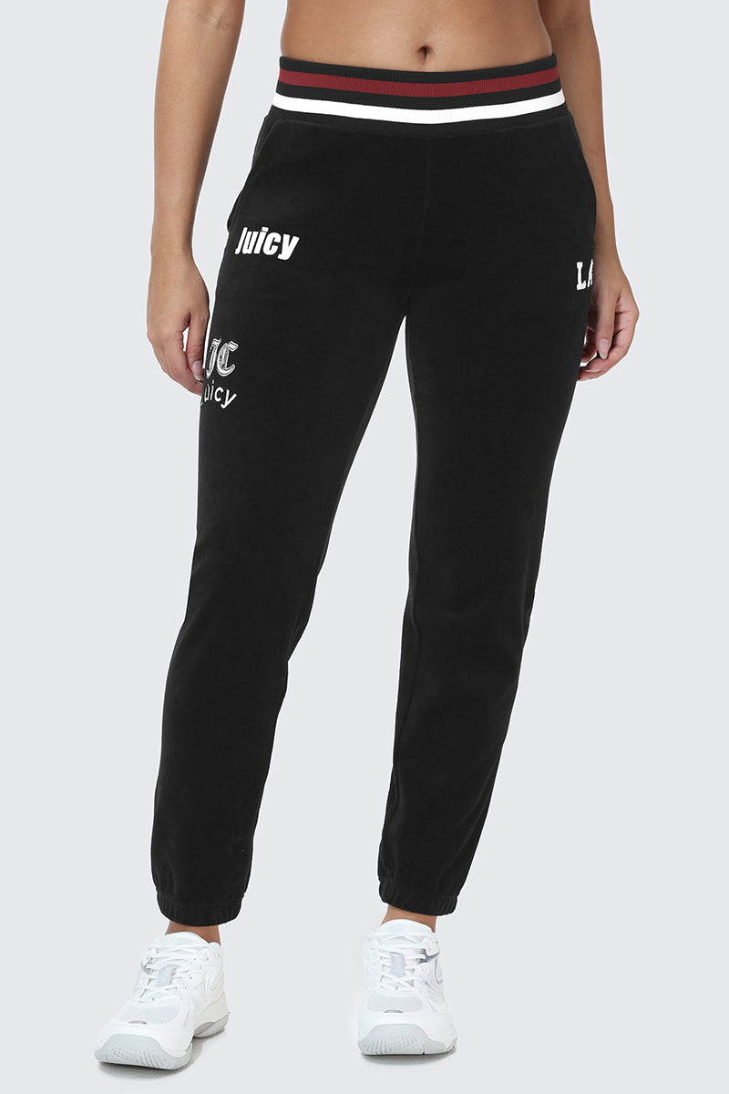Wearing the Mixed Logo Cotton Velour Jogger—featuring black velour fabric, Juicy text on the left thigh and hip, a bold red-white-black striped waistband—and paired with white sneakers, this sporty look highlights only the lower body.