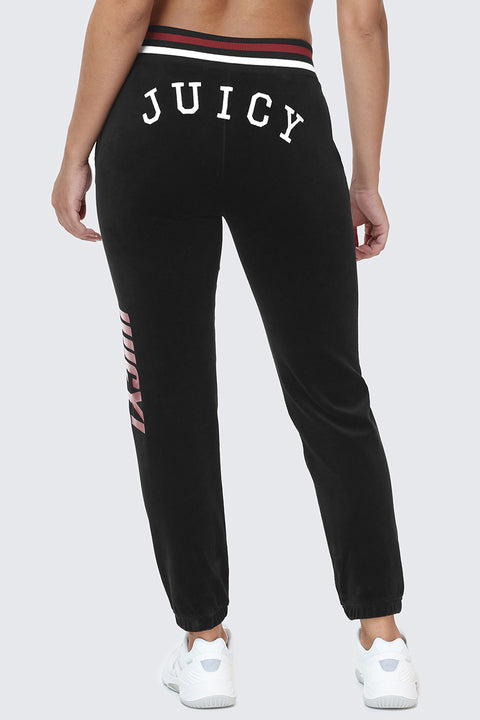 A person shown from behind wearing the Mixed Logo Cotton Velour Jogger in black with bold white "JUICY" lettering on the back, paired with white sneakers—a true sporty staple.