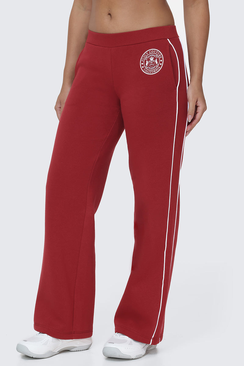 A person wears Scottie Fleece Wide Leg Pants in red with white side stripes, paired with white sneakers and featuring a collegiate-inspired Juicy logo on the upper left thigh, standing against a plain light background.