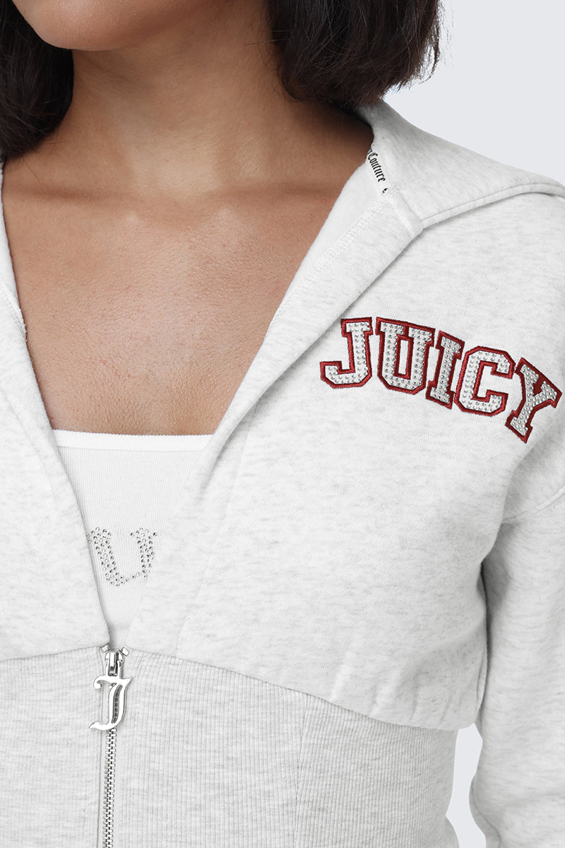 A woman wears a light gray Small Bling Fleece Quarter Zip Hoodie by Juicy Couture, featuring 'JUICY' in red letters across the chest, layered over a white tank top. The fitted hoodie is zipped partway down, revealing the neckline and some text on the tank top underneath.
