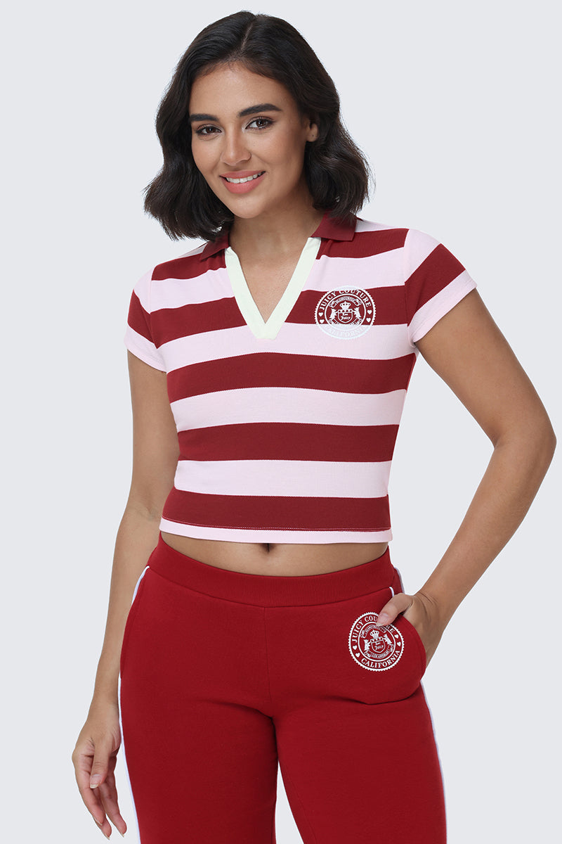 A woman wearing the Stripe Scottie Baby Polo—featuring short sleeves, a collar, and red and light pink stripes in a cropped silhouette—paired with matching red pants, smiles with one hand in her pocket.