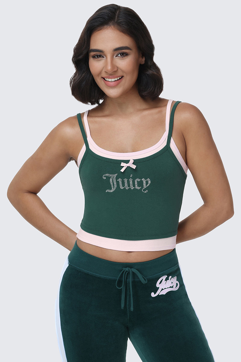 Wearing the Small Bling Double Layer Cami in green, which features a rhinestone Juicy logo and light pink trim, along with matching green pants trimmed in pink, a woman stands smiling against a plain light background.