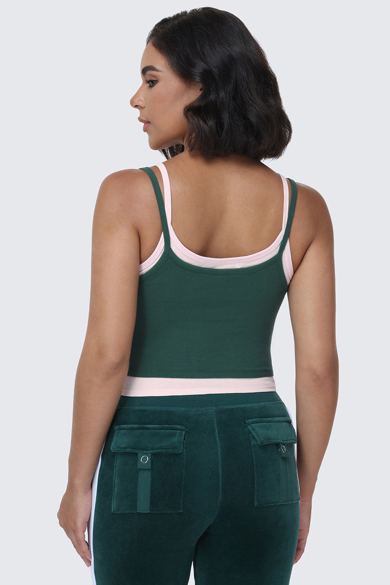 A woman with short dark hair wears the Small Bling Double Layer Cami in dark green with light pink trim, paired with matching green pants featuring back pockets adorned with a rhinestone Juicy logo, shown from behind against a light gray background.