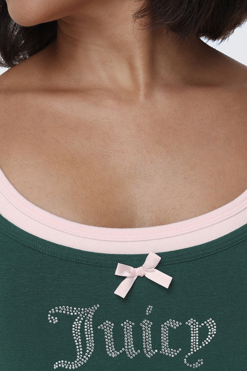 A close-up of a woman’s neck and upper chest. She is wearing the Small Bling Double Layer Cami, featuring green fabric with layered detailing, rhinestone Juicy logo lettering, pink trim underneath, and a small pink bow at the neckline.