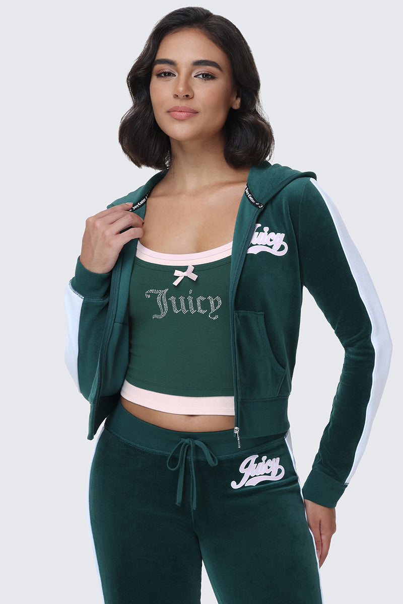 A woman stands confidently with her jacket open, looking at the camera, wearing a green velour tracksuit with white stripes and Juicy bottoms, paired with the Small Bling Double Layer Cami in pink.