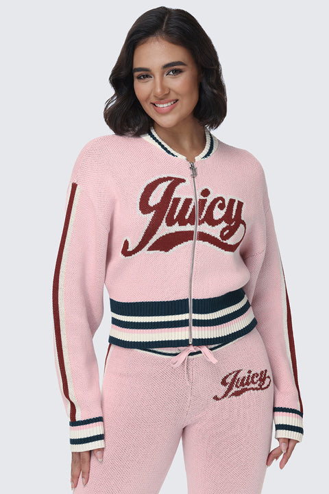 A woman stands and smiles against a plain background, wearing the Contrast Knit Bomber Jacket in pink—a zip-up sweater with Juicy script logos on both the jacket and matching pants, finished with varsity-inspired striped detailing on the sleeves, hem, and waistband.