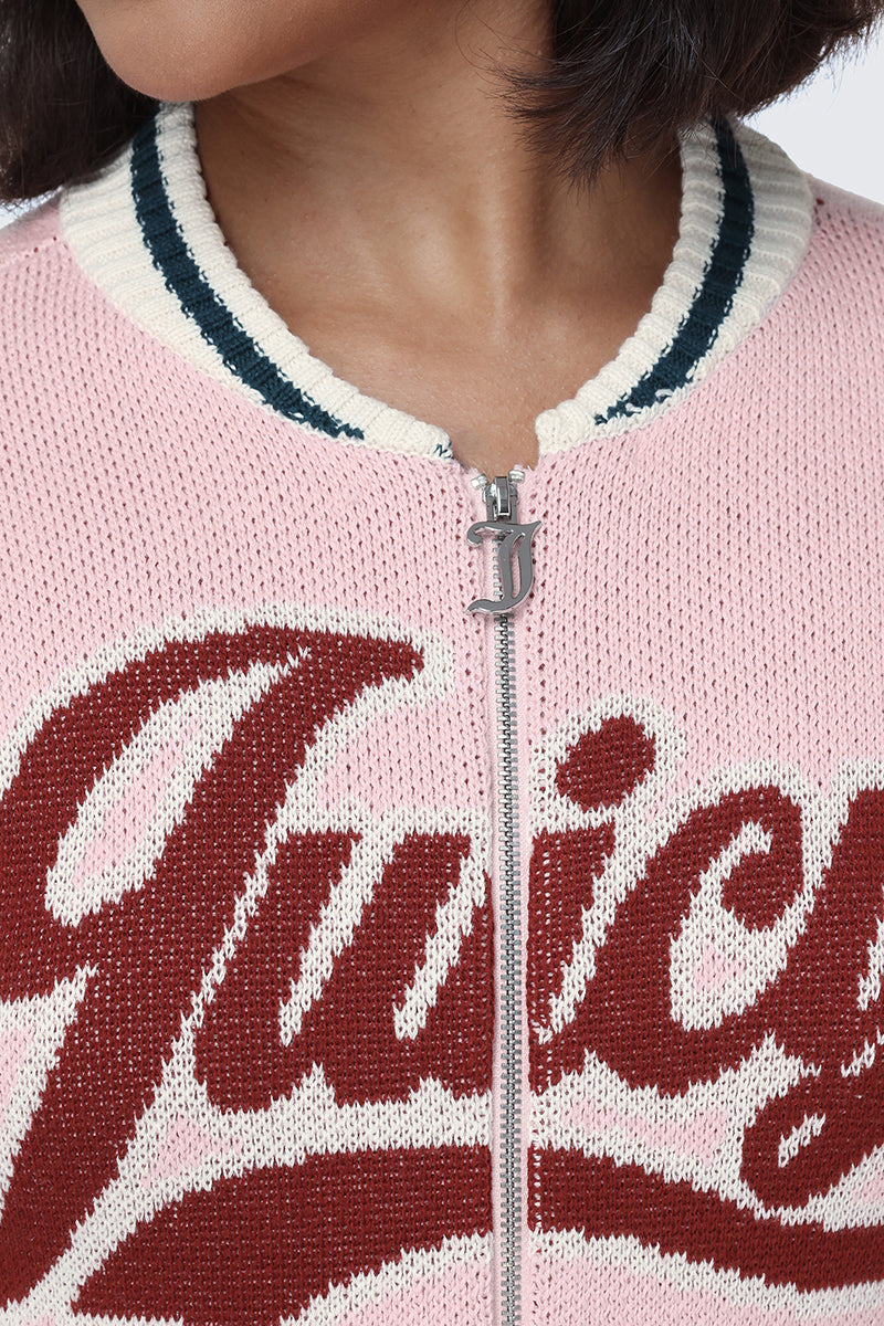 A close-up of a person wearing the Contrast Knit Bomber Jacket—a pink knit bomber jacket with white trim, a silver zipper, and the Juicy script logo partially visible in large red cursive letters across the front.