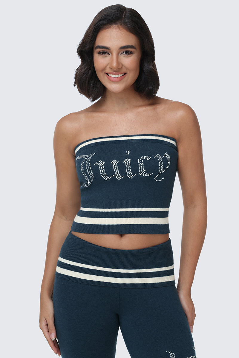A woman with short dark hair is standing and smiling at the camera, wearing a navy blue Big Bling Tube Top featuring a rhinestone logo and matching high-waisted pants with white stripes.