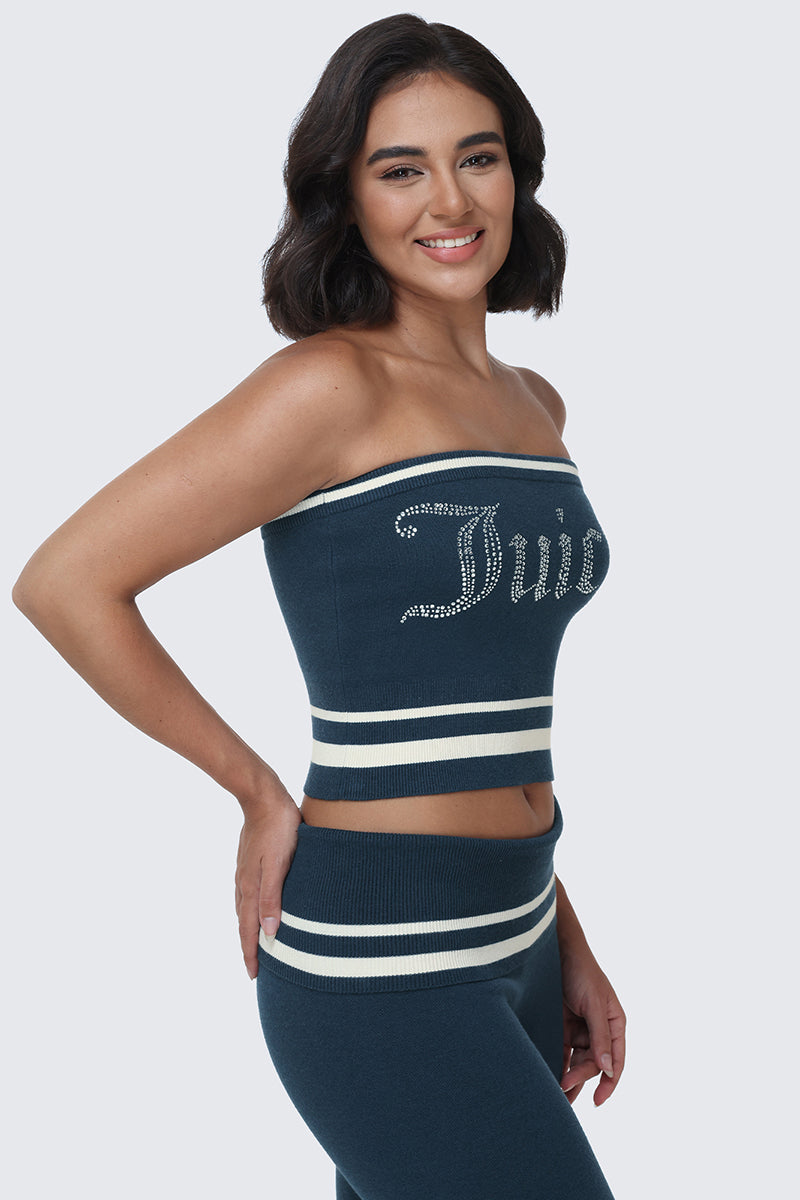 A woman with dark hair smiles, wearing the Big Bling Tube Top in blue with white stripes and a sparkling rhinestone logo, paired with matching blue pants featuring white stripes at the waist, standing against a plain light background.