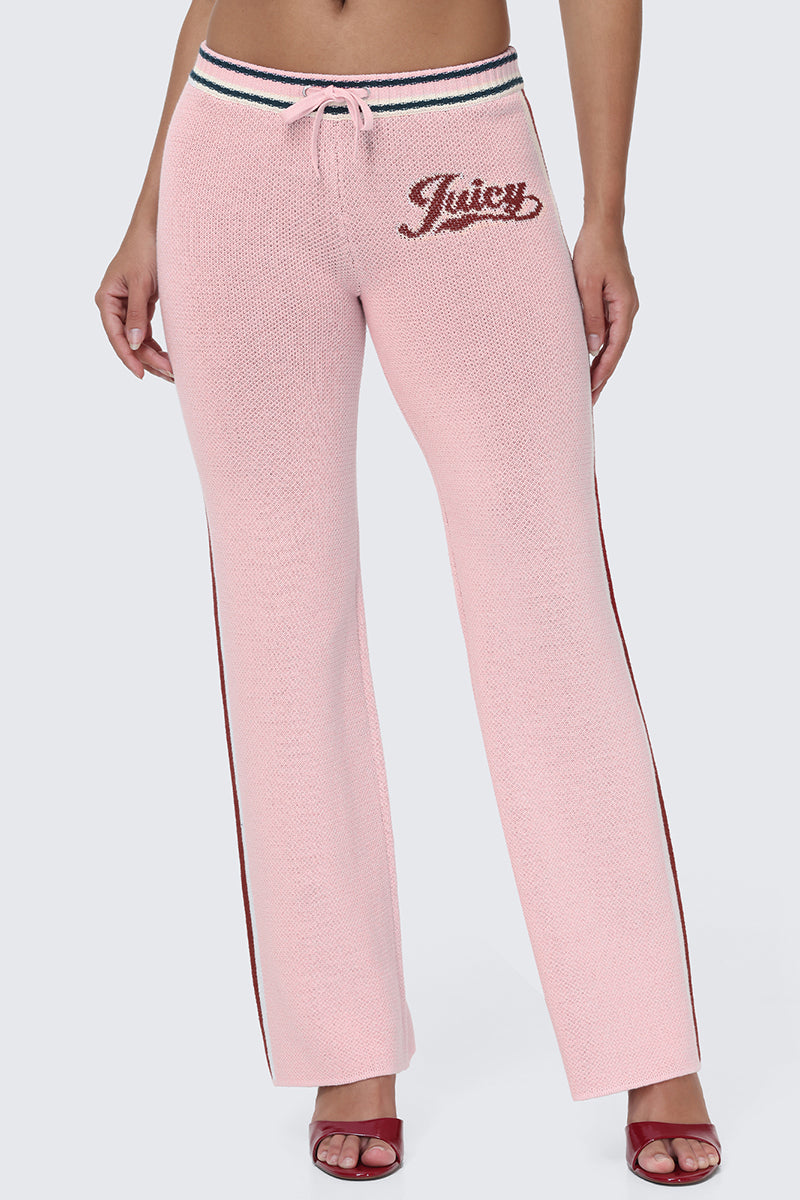A person is wearing the Contrast Knit Wide Leg Pants, featuring a light pink knit fabric, wide legs, drawstring waist, Juicy script logo on one hip, and sporty side stripes. Paired with red open-toe heels, only the lower body is visible against a plain background, letting these standout pants take center stage.