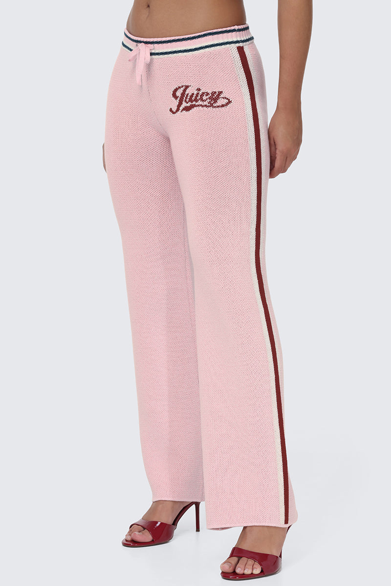 A person wearing the Contrast Knit Wide Leg Pants in light pink, featuring the iconic Juicy script logo on the side, maroon and white contrast side stripes, a drawstring waist, and paired with red heeled sandals—perfectly showcasing this sporty essential. The person's upper body is mostly out of frame.