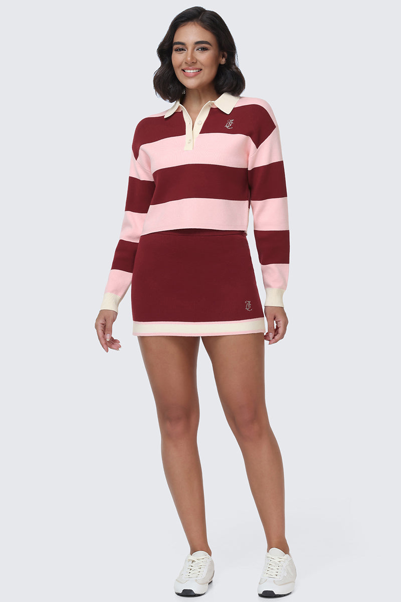 A woman smiles while wearing the Small Bling Knit Mini Skirt in maroon with a crisp white contrast hem, paired with a maroon and pink striped long-sleeve polo and white sneakers, standing against a light gray background.