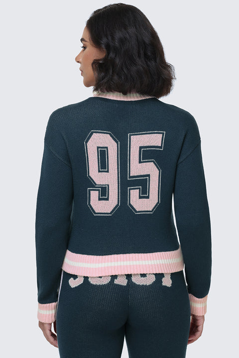 A woman with shoulder-length dark hair is shown from the back, wearing a dark Collegiate Knit Bomber Jacket by Juicy Couture featuring a pink "95" on the back, paired with matching pants with pink trim and text.