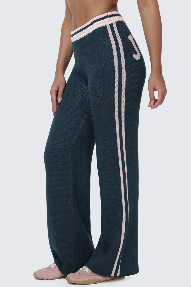 Wearing the Collegiate Knit Wide Leg Pants—high-waisted, dark teal knit wide legs with pink and white side stripes, varsity-style logo detailing including a letter J near the waistband—paired with pink sneakers.