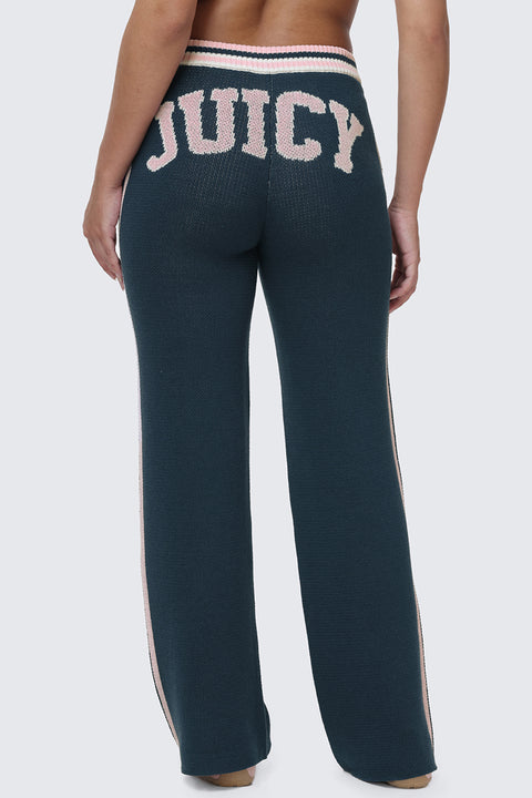 A person stands facing away, wearing Collegiate Knit Wide Leg Pants in dark blue, featuring bold "JUICY" lettering in large pink letters across the back for standout logo detailing.