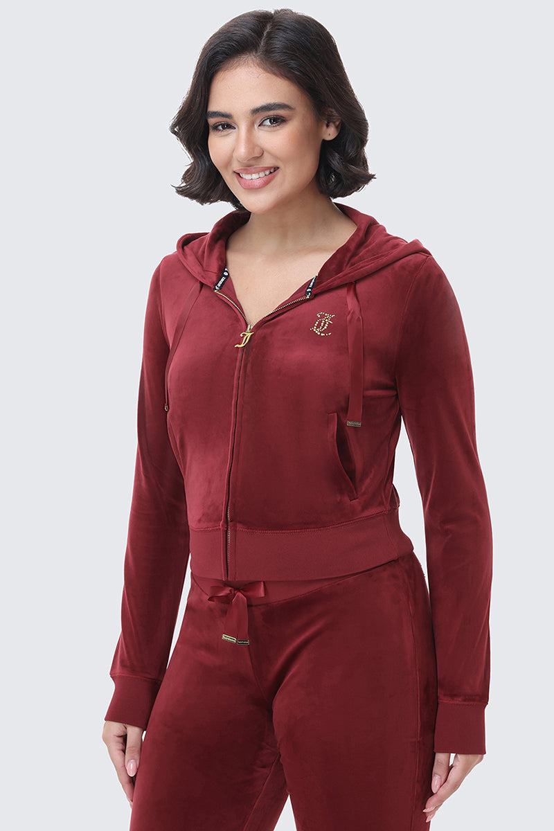 A woman wearing a deep red, fitted OG Big Bling Ribbon Hoodie featuring a zippered front, gold hardware, and a small jeweled emblem on the chest.