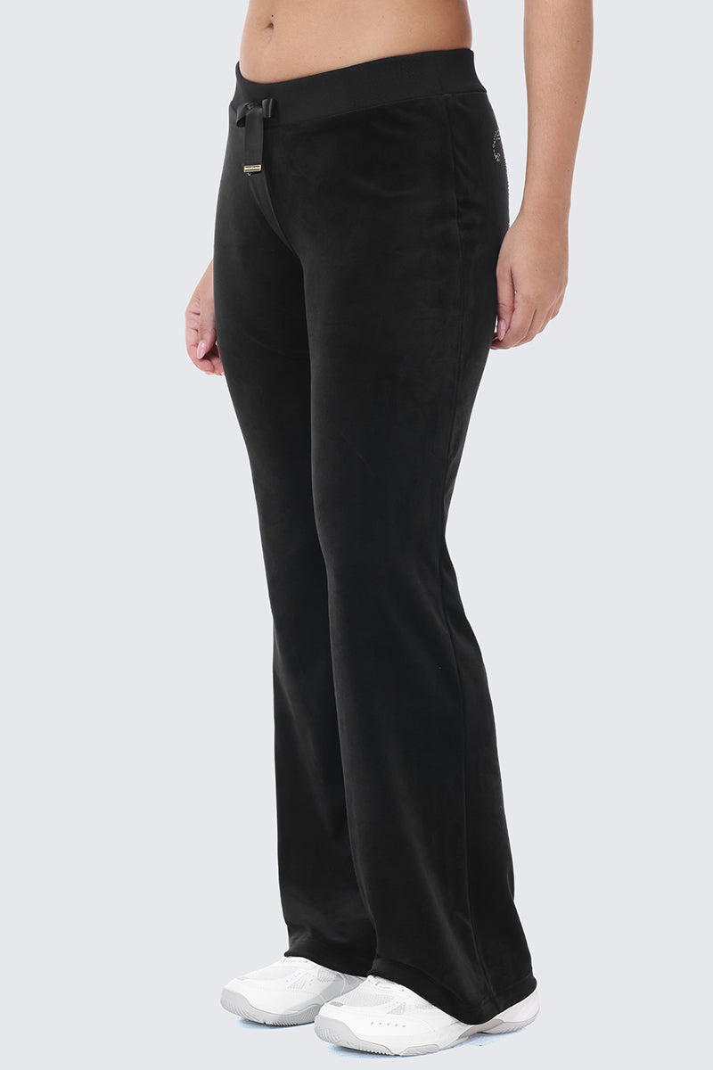 Side view of black velour OG Big Bling Ribbon Track Pants with ribbon details, a drawstring waistband, and white sneakers.