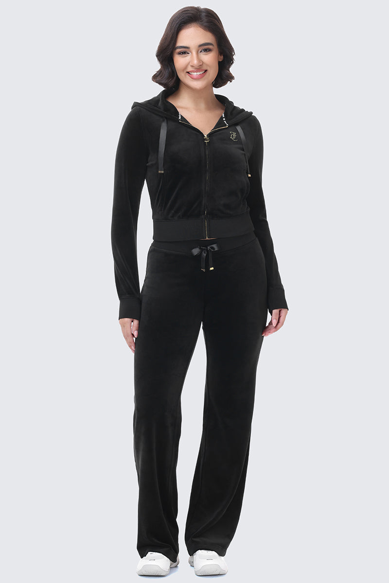 A smiling woman wearing a black zip-up hooded jacket and matching OG Big Bling Ribbon Track Pants with ribbon details.