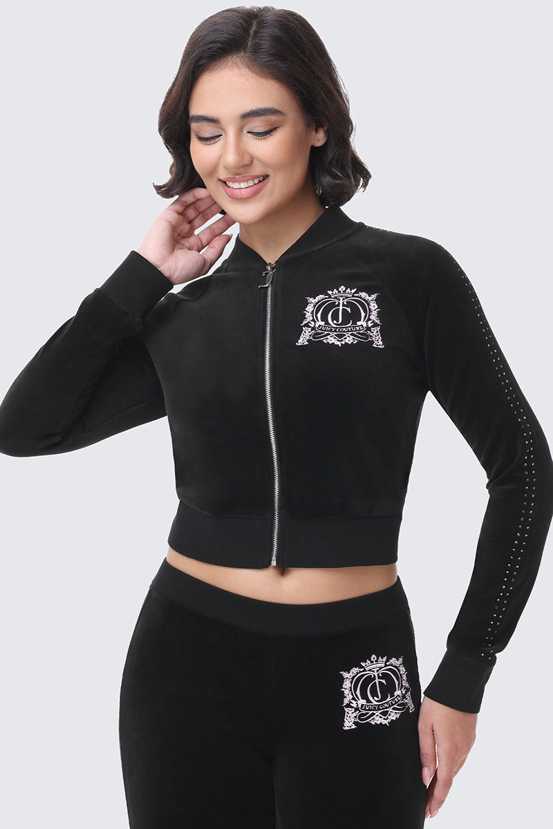 A person wearing a black Scottie Crown Cotton Velour Jacket with a cropped, sporty silhouette, featuring a rhinestone-studded crown logo on the chest and a line of rhinestones running down the sleeves.