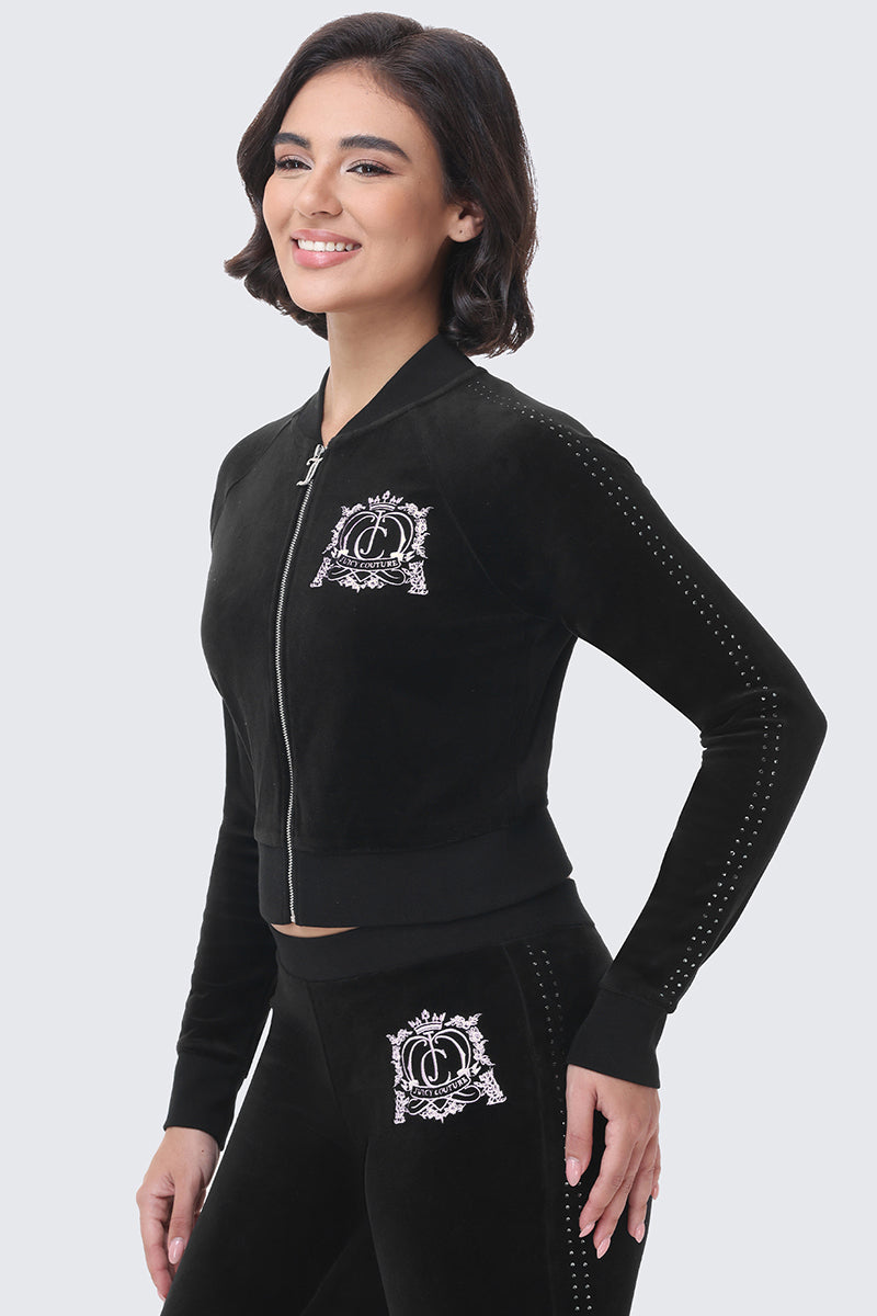 A woman wears a black Scottie Crown Cotton Velour Jacket featuring a white crown emblem on the chest with matching pants for a sporty silhouette.