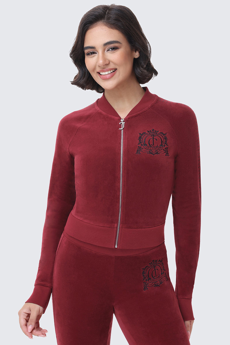 A smiling woman wears a burgundy Scottie Crown Cotton Velour Jacket with a black embroidered crown logo on the chest and matching sweatpants in a sporty silhouette.