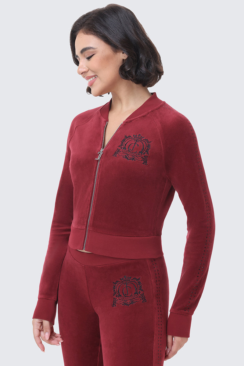A woman wearing a burgundy Scottie Crown Cotton Velour Jacket with a black embroidered crest on the chest and matching track pants.