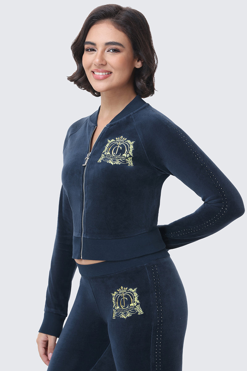 A person wears a navy blue cotton velour Scottie Crown Cotton Velour Jacket featuring a yellow crown emblem on the chest and dotted detailing along the sleeves.