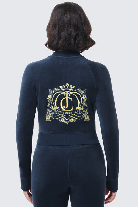 Back view of a person wearing a dark blue Scottie Crown Cotton Velour Jacket, featuring a gold embroidered crest and the Juicy Couture logo on the back.