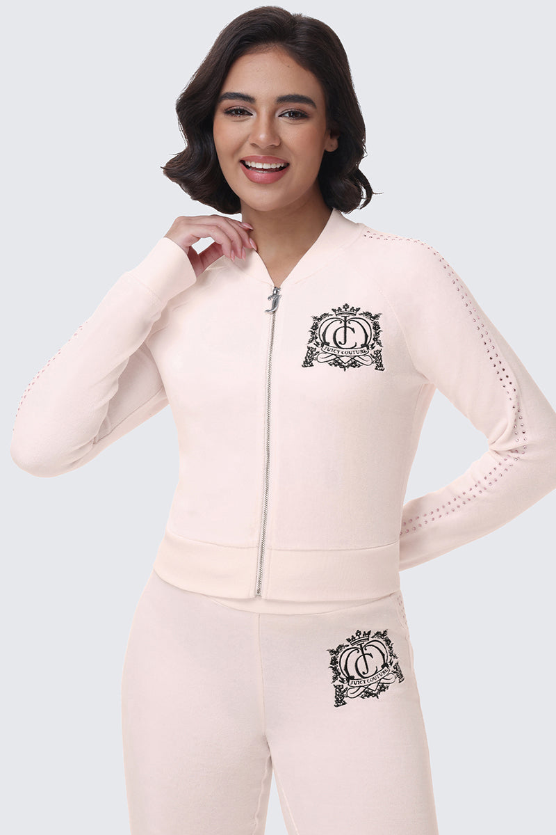 A woman wearing a pale pink Scottie Crown Cotton Velour Jacket with a crown emblem on the chest and matching pants with the same emblem at the hip for a coordinated look.
