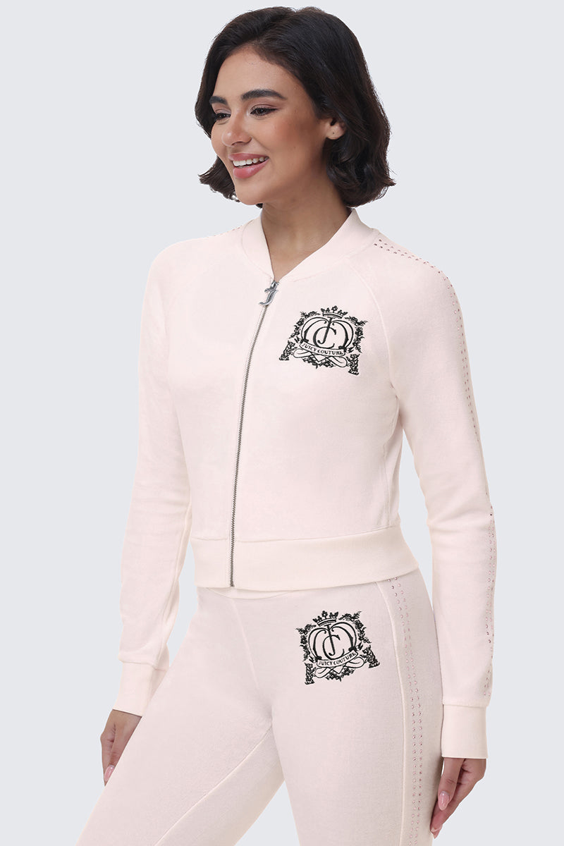 A person wearing a pale pink Scottie Crown Cotton Velour Jacket and matching pants, both featuring a dark crest logo on the chest and hip to create a coordinated look.