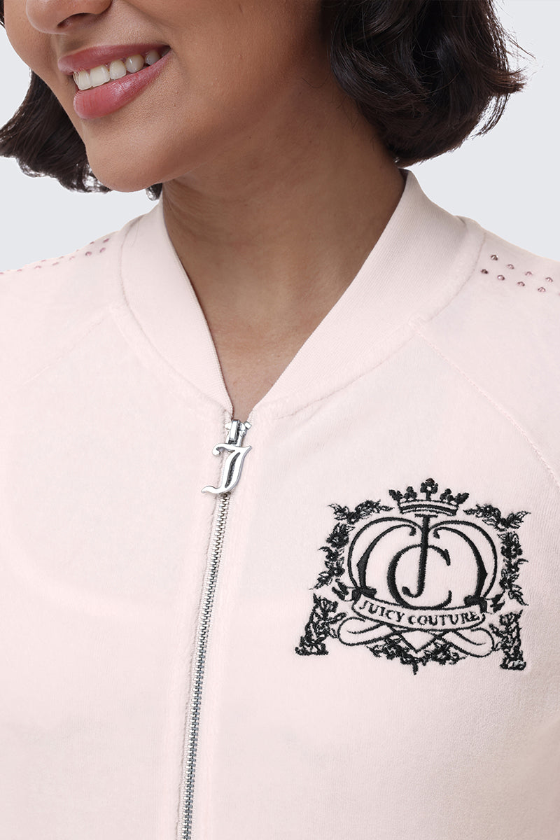 Close-up of a pale pink Scottie Crown Cotton Velour Jacket featuring a black embroidered crest logo on the chest and a metallic J zipper pull.
