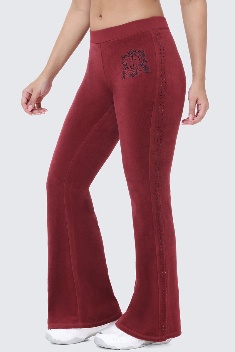 Scottie Crown Cotton Velour Track Pants in deep red, featuring a flared silhouette, a black crown graphic on the hip, and a vertical line of small studs along the side.