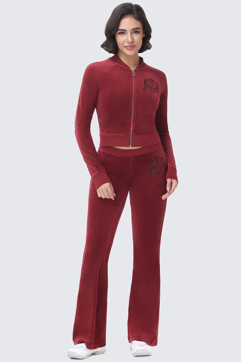 A woman wears a matching deep red velour track jacket and Scottie Crown Cotton Velour Track Pants, both featuring a dark circular crest logo in a sporty flared silhouette.
