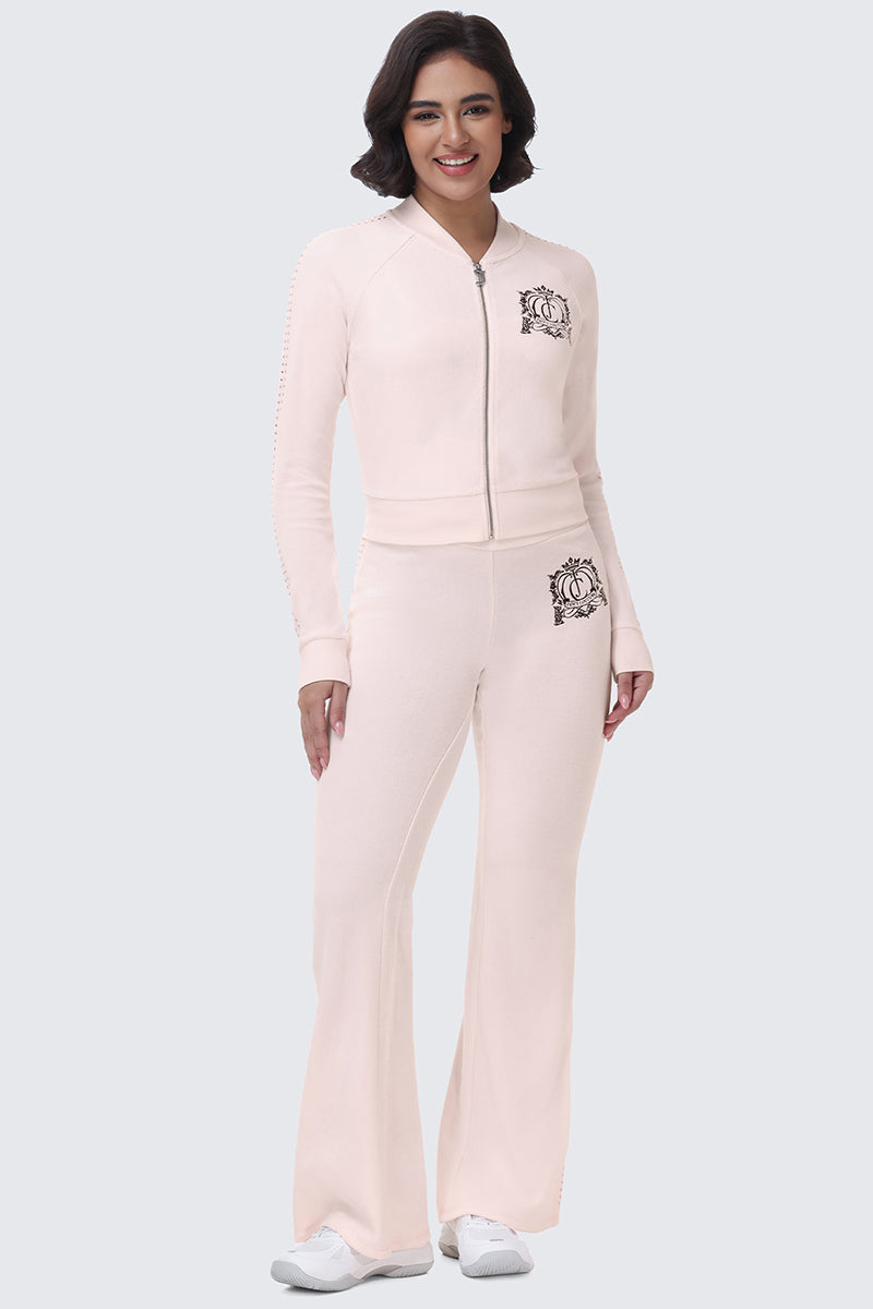 A person wears a pale pink zip-up track jacket and matching Scottie Crown Cotton Velour Track Pants, both featuring a decorative crown crest logo in a sporty silhouette.