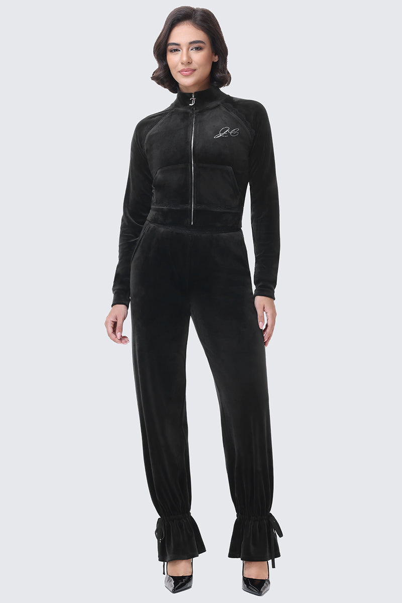 A woman wears a black Small Bling Velour Jacket and matching high-waisted pants with ruffled, cinched hems in a Y2K-inspired style.
