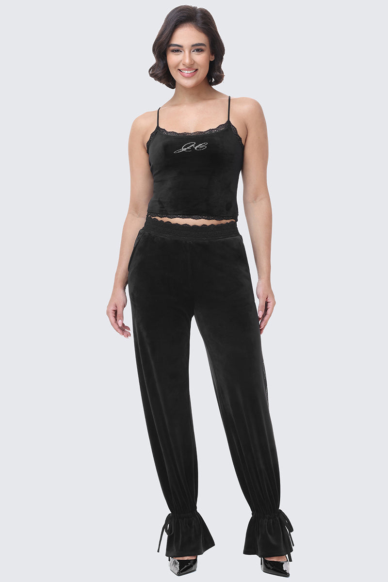 A woman wearing a black Juicy Couture velour camisole with lace trim and matching Small Bling Velour Track Pants featuring ruffled, drawstring hems.