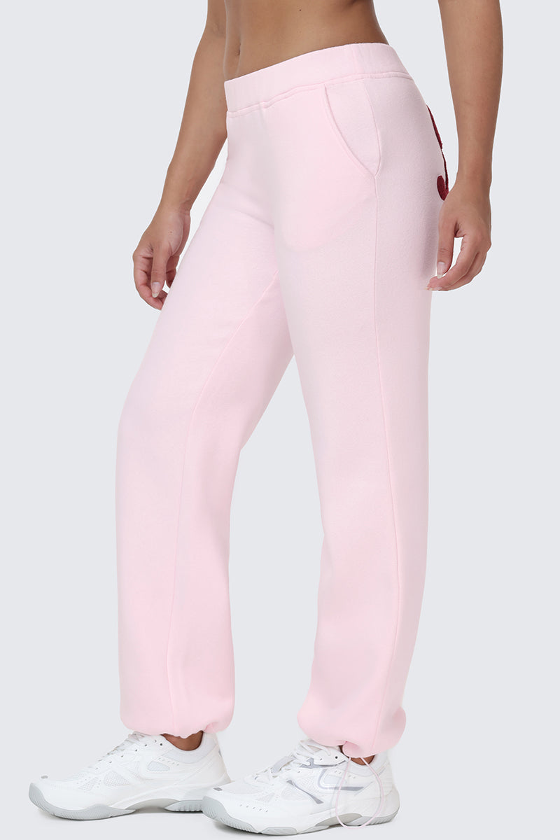 A person stands sideways wearing light pink Embroidered Knit Bubble Leg Pants and white sneakers. Their face is not visible, and the background is a plain light gray.