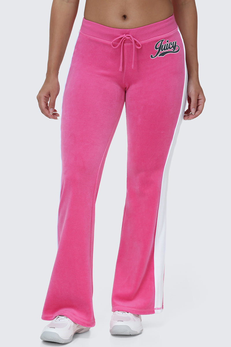 A person wearing the Cotton Velour Track Pants in pink, featuring plush cotton velour fabric, white side stripes, and a Juicy logo on the left hip. The pants have flap back pockets and a relaxed fit, styled with white sneakers for the perfect off-duty look. The upper body is not visible.