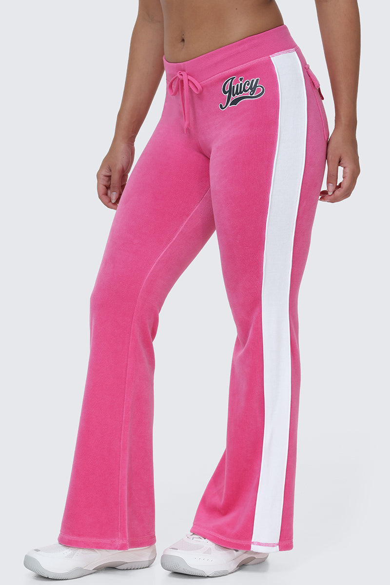 A person wearing the Cotton Velour Track Pants in pink, featuring a white side stripe, flap back pockets, white sneakers, and "Juicy" embroidered on the hip creates an effortlessly cool off-duty look.