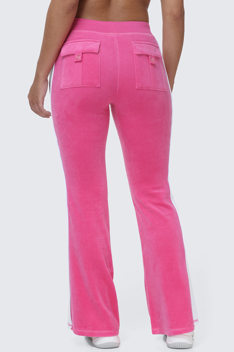 A person models the Cotton Velour Track Pants in bright pink, featuring flap back pockets, paired with white sneakers and photographed from behind against a plain light gray backdrop for an effortless off-duty vibe.