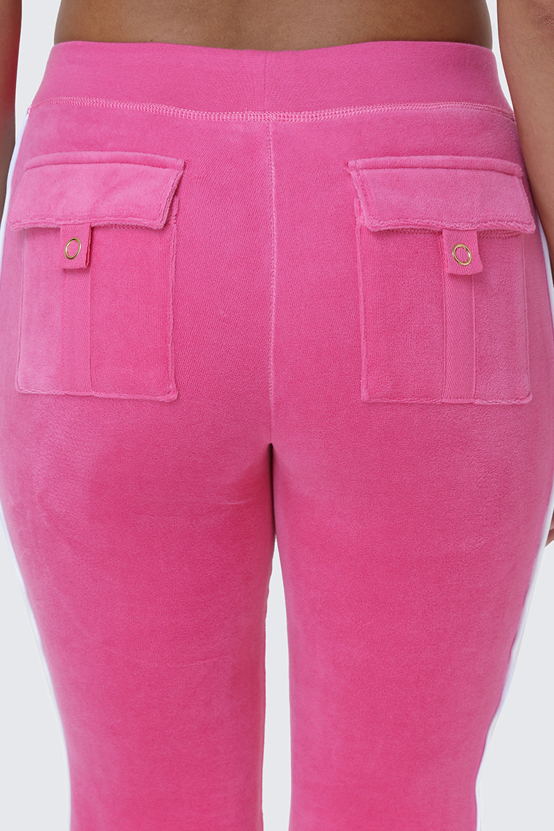 Close-up of the back of a person wearing Cotton Velour Track Pants in vibrant pink, featuring flap back pockets secured with gold buttons—ideal for creating an effortlessly chic off-duty style.