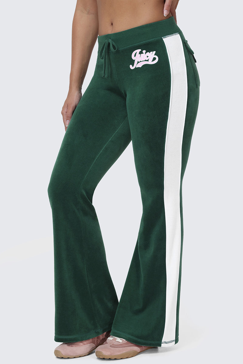 A person wearing Cotton Velour Track Pants with flap back pockets, white side stripes, the Juicy logo on the hip, and pink sneakers.
