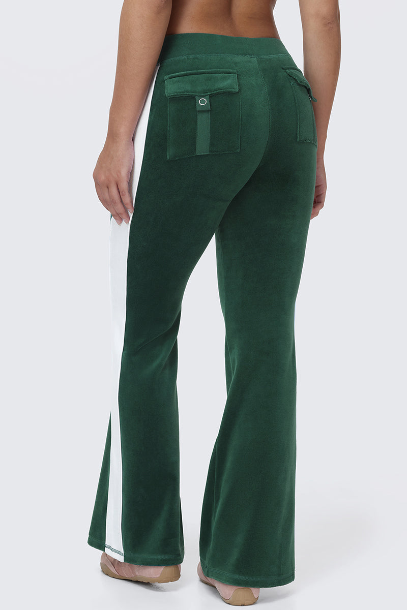 Wearing Cotton Velour Track Pants in green with white side stripes and flap back pockets, paired with tan sandals, this person stands against a plain light background, capturing an effortlessly cool off-duty vibe.