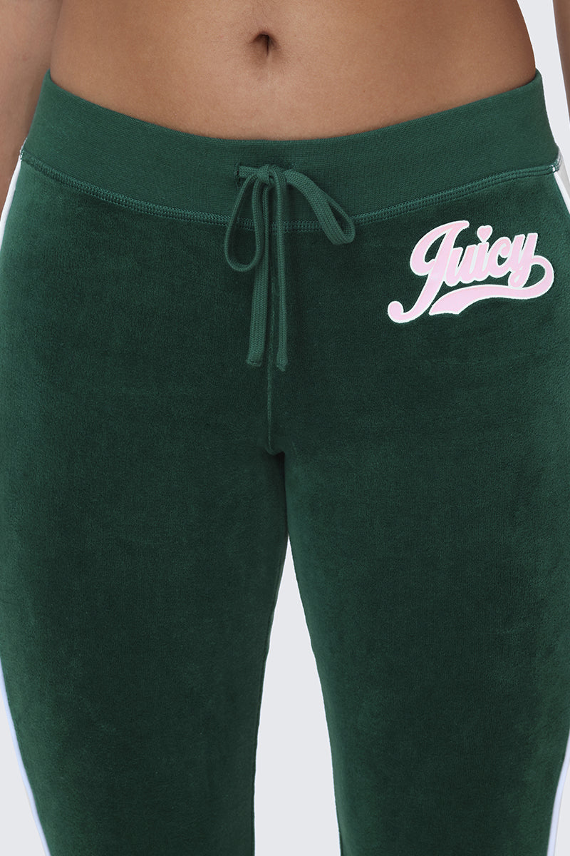 A person wearing Cotton Velour Track Pants in dark green, featuring a drawstring waist, stylish flap back pockets, and "Juicy" written in pink on the left hip.