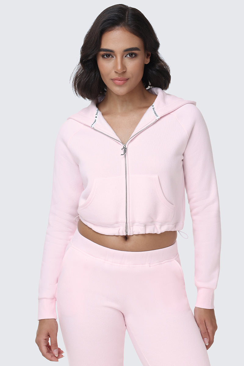 A woman wearing an Embroidered Knit Cropped Hoodie in light pink with matching sweatpants stands against a plain gray background, looking confidently at the camera.